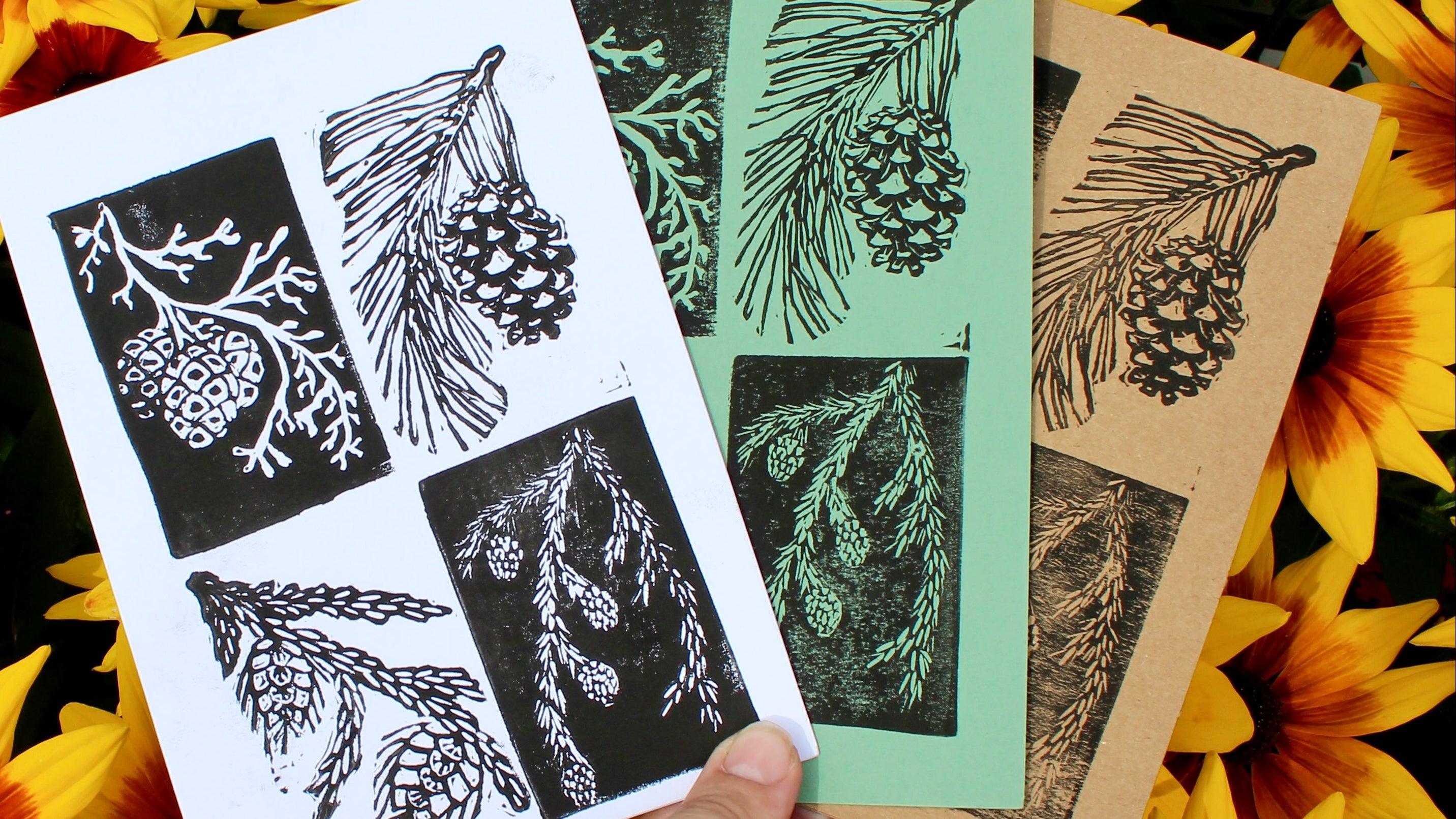 Hand holding prints of nature-themed designs against a background of sunflowers